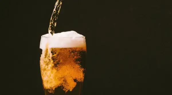 Birra dorata versata in un bicchiere, con schiuma abbondante e bollicine che salgono. Un piacere rinfrescante, ricco di sali minerali.