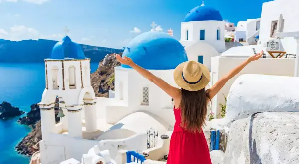 Santorini w kwietniu zachwyca! Kobieta w czerwonej sukience i kapeluszu cieszy się idealną pogodą, podziwiając białe domy i niebieskie kopuły.