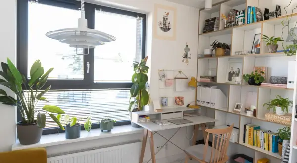 Jasny gabinet w domu z biurkiem, regałem pełnym książek i roślin. Inspiracje do aranżacji domowego biura.