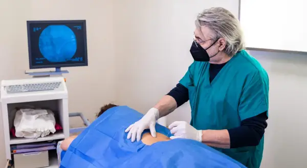 Un médecin réalise une infiltration du dos guidée par imagerie. Le patient est allongé, couvert d'un drap bleu.