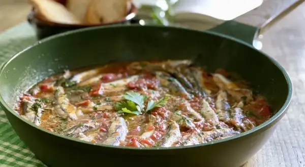 Un saporito bagnun di acciughe in padella, con pomodoro e prezzemolo, pronto per essere gustato con pane tostato.