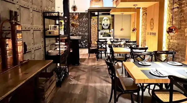 Interior de un bistro bar con mesas puestas, sillas de madera oscura y decoración industrial.