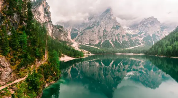 Spokojne Lago di Braies odbija majestatyczne góry i zielone lasy. Ścieżka wije się wzdłuż skalistego brzegu.