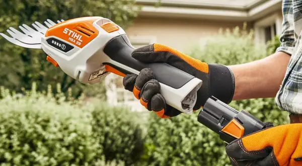 Ręka w rękawicy zakłada baterię do nożyc akumulatorowych do trawy Stihl HSA 26, gotowa do przycinania.