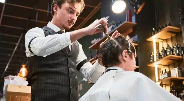 Elegancki barber z wąsikiem precyzyjnie ścina włosy klienta. Kto to? Mistrz fryzjerstwa!