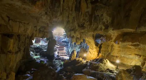 Interior de la cueva del Pindal, con estalactitas, rocas y escaleras iluminadas que conducen a la salida.
