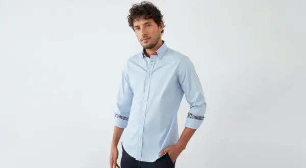 Ein Mann trägt ein hellblaues Hemd mit floralen Akzenten an Kragen und Manschetten. So lässt sich ein hellblaues Hemd kombinieren.