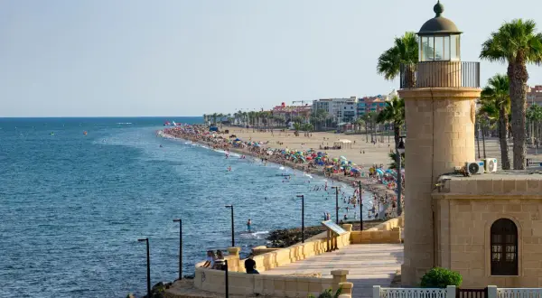Faro y playa abarrotada en el paseo marítimo de Roquetas de Mar. Gente disfrutando del sol y el mar.