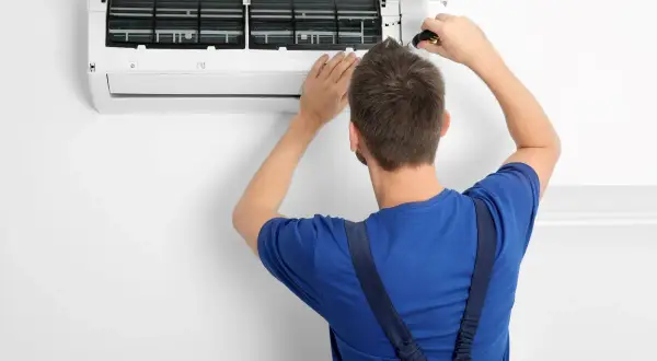 Tecnico con cacciavite apre un condizionatore per manutenzione. Il significato di "heat condizionatore" è la sua capacità di riscaldare.