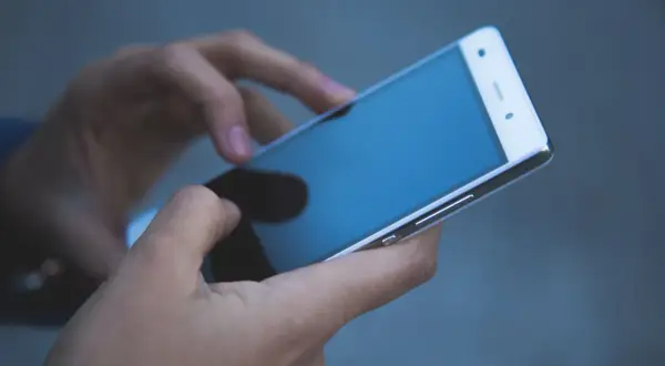 Dłonie trzymają smartfon, być może szukając informacji, jak wyłączyć pocztę głosową.