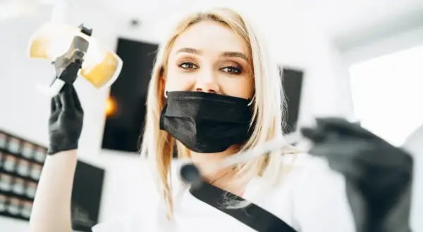 Uśmiechnięta dentystka w masce przygotowuje się do lakierowania zębów, trzymając lampę i narzędzia.