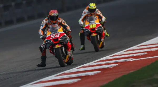 Dos pilotos de MotoGP compiten en una carrera. El piloto número 93 de Repsol Honda lidera, seguido de cerca por el piloto número 36. El coste de una moto de MotoGP es altísimo.