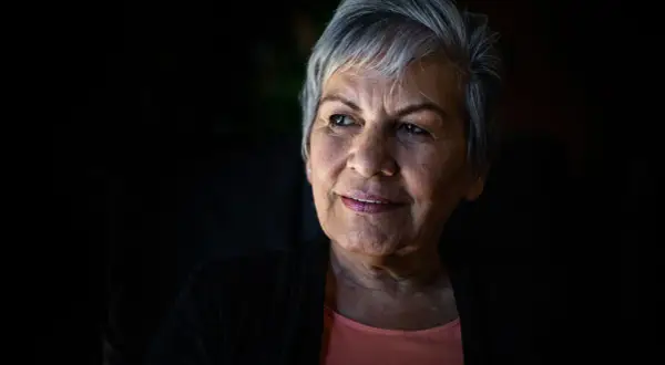 Portret starszej kobiety z siwymi włosami, patrzącej w bok z lekkim uśmiechem.