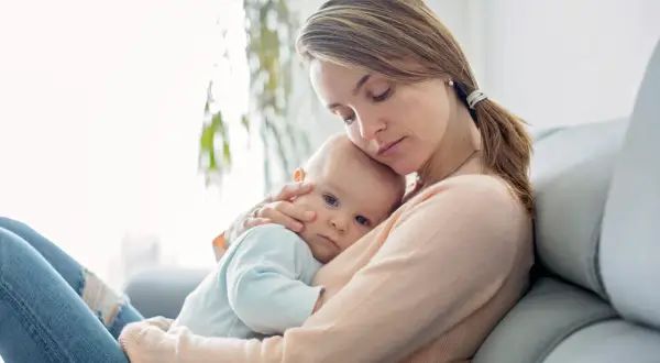 Matka tuli dziecko, które ma jelitówkę u niemowlaka. Widać troskę na jej twarzy.