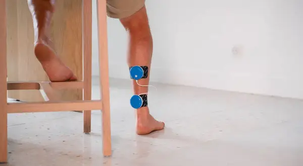 Un coureur souffrant de douleur au tendon d'Achille utilise un appareil d'électrostimulation pour soulager sa blessure.