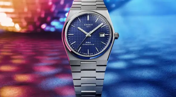 Reloj Tissot 1853 PRX Powermatic 80 con esfera azul texturizada y brazalete metálico, sobre un fondo vibrante de luces. Descubre su tissot 1853 precio.