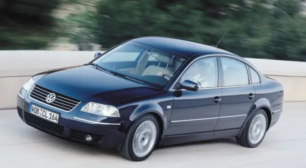 Ciemnoniebieski VW Passat W8 z jasnym wnętrzem mknie po drodze, za kierownicą siedzi mężczyzna.