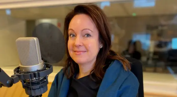 Anna Borg ler mot kameran i en inspelningsstudio, med en mikrofon framför sig.