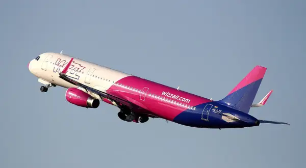 Samolot Wizz Air w różowo-niebieskich barwach wznosi się na tle błękitnego nieba.