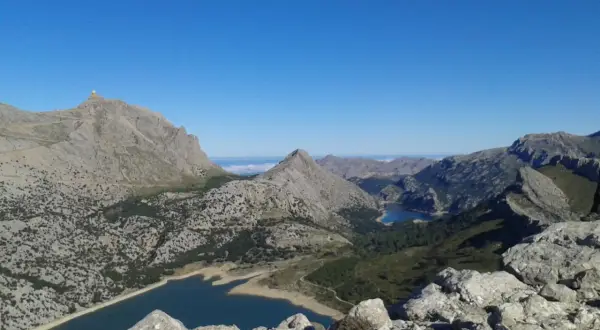 Vistas impresionantes desde el Puig de sa Rateta, con embalses y montañas escarpadas bajo un cielo azul.