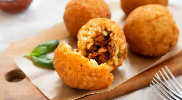 Arancini dorés et croustillants, une recette sicilienne à déguster. Un est un arancino ouvert révèle sa garniture savoureuse.