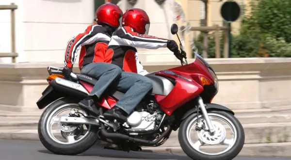 Dwie osoby w czerwonych kaskach i kurtkach jadą na czerwonym motocyklu. To świetna kategoria a1 dla miłośników wolności.