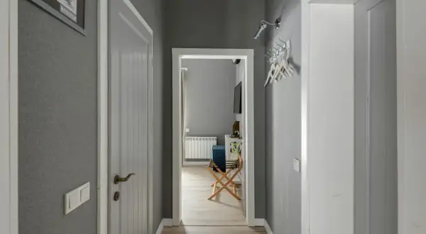Pasillos con encanto, con paredes grises, puertas blancas y un cuadro en la pared. Se vislumbra una habitación con un radiador y un banco.