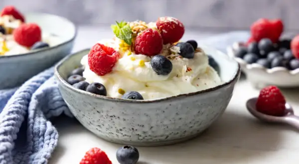 Cremiger frozen Joghurt mit frischen Himbeeren und Blaubeeren, garniert mit Minze und Nüssen. Ein erfrischender Genuss.