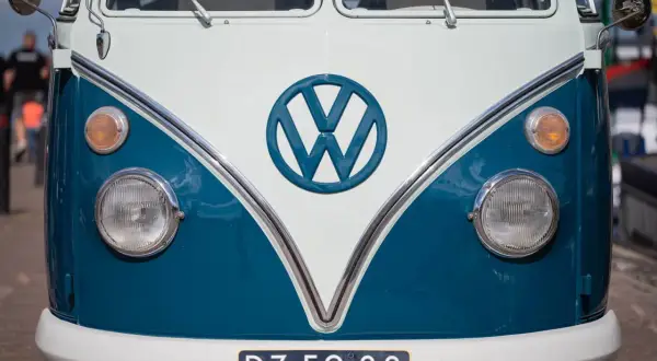 Przód klasycznego VW T2 w kolorze białym i niebieskim. Charakterystyczne okrągłe logo VW i okrągłe reflektory.