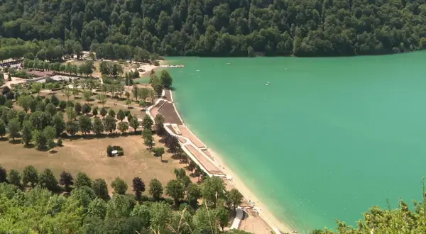 Vue aérienne d'un magnifique lac aux eaux turquoise, idéal pour la baignade. Des plages aménagées bordent la rive, entourées de verdure et d'arbres.