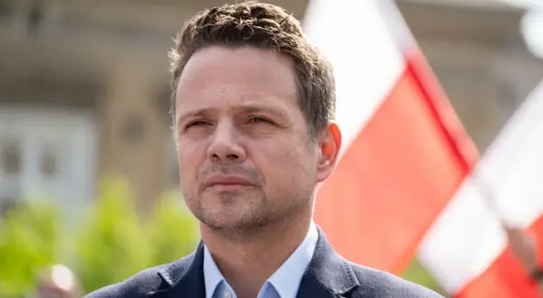 Rafał Trzaskowski, którego wiek jest często dyskutowany, na tle biało-czerwonych flag.