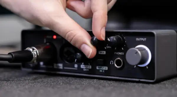 Dłoń kręci pokrętłem "MIX" na interfejsie audio, przygotowując się do podłączenia telefonu do wzmacniacza.
