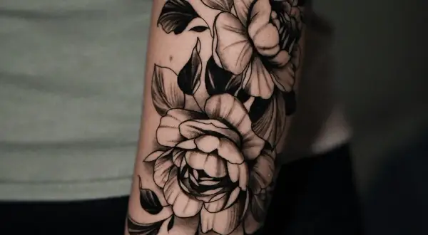 Un primer tatuaje de peonías en blanco y negro, detallado y artístico, adornando un brazo.