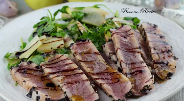 Deliziosa tagliata di tonno scottata, cosparsa di semi di sesamo nero, servita con un'insalata fresca di rucola e scaglie di parmigiano.
