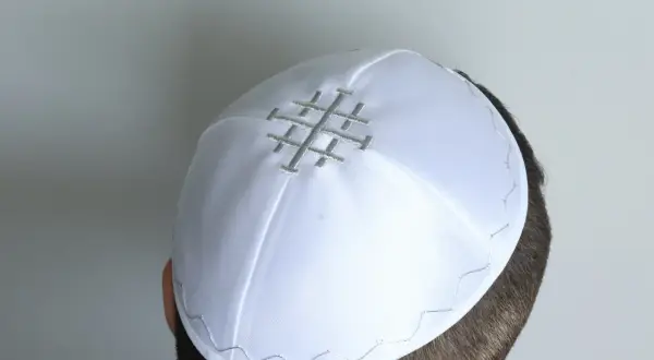 Biała czapka z symbolem Jerozolimy, noszona przez mężczyznę. To może być czapka proboszcza, symbolizująca jego posługę.