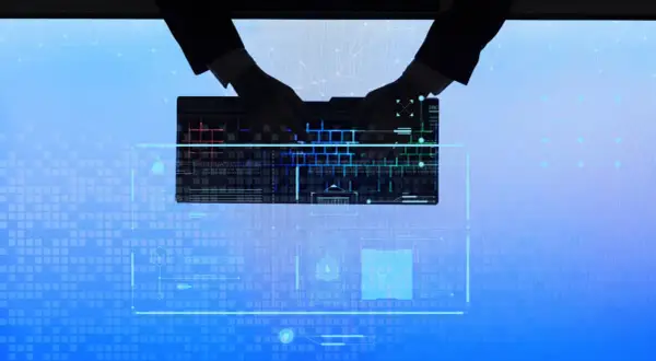 Dłonie w rękawiczkach piszą na podświetlanej klawiaturze, tworząc tło dla cyfrowego świata, gdzie czai się cyberprzestępczość.