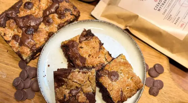 Pyszne brookies z kawałkami czekolady, obok maliny i opakowanie ciemnej czekolady.