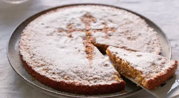 Tarta de Santiago, espolvoreada con azúcar glas, con una porción servida.
