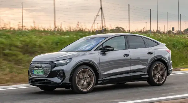 Szary Audi Q4 Sportback sunie po drodze, otoczony zielenią i zachodzącym słońcem.
