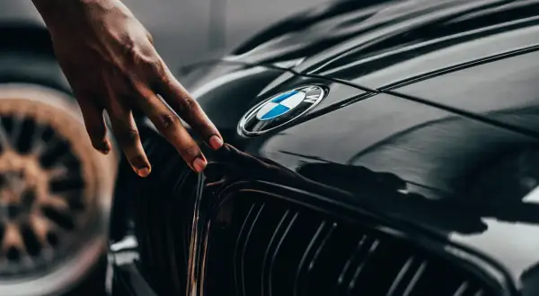 Dłoń dotyka błyszczącej maski czarnego BMW. Zastanawiasz się, ile schnie lakier bezbarwny po polerowaniu?