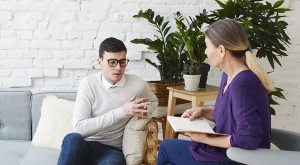 Mężczyzna w okularach rozmawia z kobietą, która notuje. To typowa scena, gdy psychoterapeuta pomaga pacjentowi.