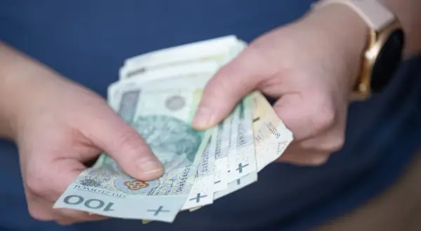 Dłonie trzymające banknoty 100 zł. Czy to już czas na rozliczenie podatku od wygranej?