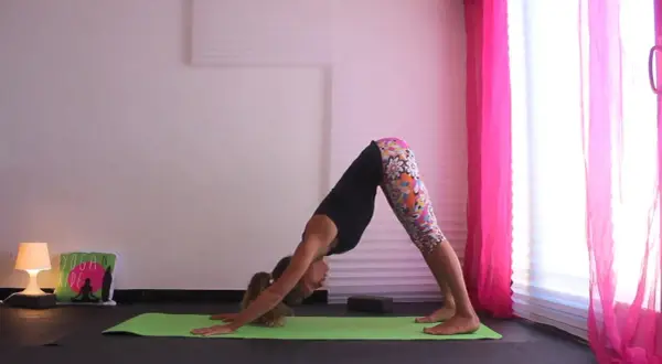 Donna in posizione di Urdhva Mukha Svanasana su un tappetino verde, con leggings colorati e uno sfondo rosa.
