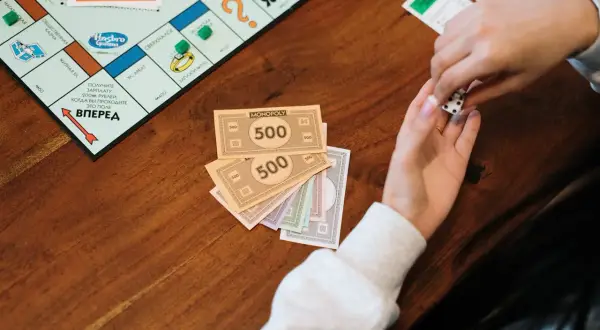Ręce trzymają kości i pieniądze z gry Monopoly. Naucz się, jak rozdawać pieniądze w Eurobiznes, by wygrać!