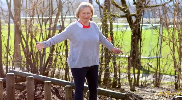 Ältere Frau balanciert auf Holzstämmen im Freien.