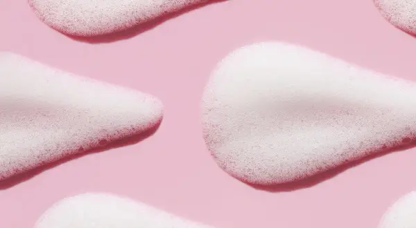 Delikatna piana z disodium laureth sulfosuccinate na różowym tle, tworząca miękkie, faliste kształty.