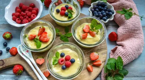Vier Gläschen cremiger Vanillepudding, garniert mit frischen Erdbeeren, Himbeeren und Blaubeeren. Ein süßer Genuss!