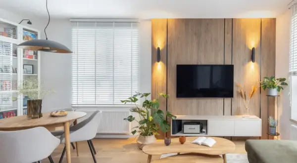 Przytulny salon inspiracje: drewniana ściana z TV, okrągły stół z krzesłami, rośliny i stylowe oświetlenie tworzą ciepłą atmosferę.
