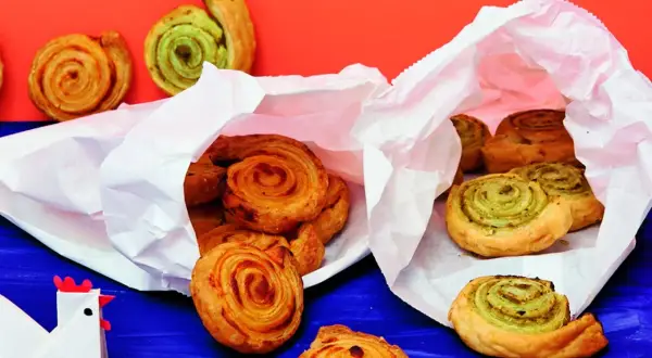 Zwei weiße Papiertüten quellen über mit köstlichen Pesto-Schnecken. Einige sind goldbraun, andere mit grünem Pesto gefüllt.