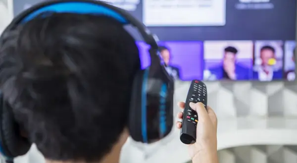 Osoba w słuchawkach trzymająca pilot do telewizora.